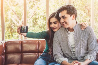 Mutlu Asyalı çift evdeki oturma odasında cep telefonuyla selfie çekmeyi sever..