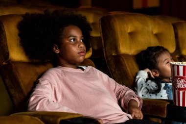 İki Afrikalı ve Asyalı çocuk sinemada eğleniyor ve film izlemekten zevk alıyor.