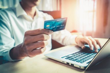 Genç adam, laptop bilgisayar başvurusu ya da web sitesinde online alışveriş yapmak için kredi kartı kullanıyor. E-ticaret ve online alışveriş kavramı.