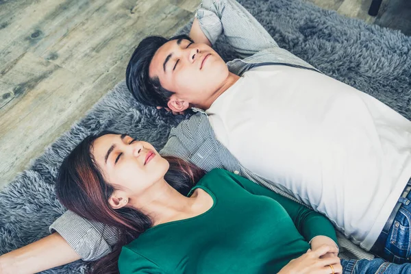 Happy Asian couple lying together on carpet at living room floor. Love relationship and lifestyle concept.