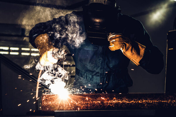 Metal welder working with arc welding machine to weld steel at factory while wearing safety equipment. Metalwork manufacturing and construction maintenance service by manual skill labor concept.