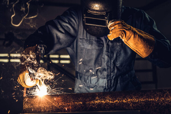 Metal welder working with arc welding machine to weld steel at factory while wearing safety equipment. Metalwork manufacturing and construction maintenance service by manual skill labor concept.