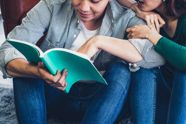 Young Asian couple reading book in living room. Love relationship and lifestyle concept.