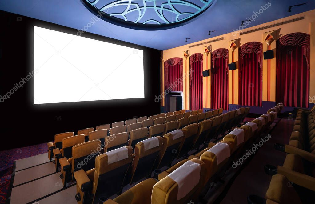 Cinema theater screen in front of seat rows in movie theater showing white screen projected from cinematograph. The cinema theater is decorated in classical style for luxury feeling of movie watching.