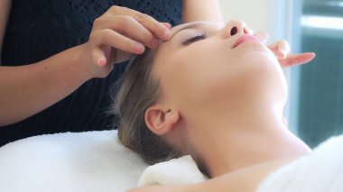 Lüks bir spa merkezinde masaj terapisti tarafından yüz masajı ve spa tedavisi için kaplıcaya uzanmış rahat bir kadın. Sağlık, stres atma ve gençleştirme kavramı.