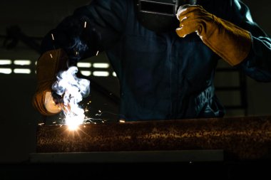 Fabrikada çelik kaynak makinesiyle çalışan metal kaynakçı güvenlik ekipmanı takıyor. El becerisi iş gücü kavramına göre metal imalatı ve inşaat bakım hizmeti.