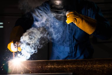 Fabrikada çelik kaynak makinesiyle çalışan metal kaynakçı güvenlik ekipmanı takıyor. El becerisi iş gücü kavramına göre metal imalatı ve inşaat bakım hizmeti.