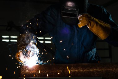 Fabrikada çelik kaynak makinesiyle çalışan metal kaynakçı güvenlik ekipmanı takıyor. El becerisi iş gücü kavramına göre metal imalatı ve inşaat bakım hizmeti.