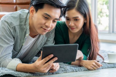 Mutlu Asyalı çift oturma odasında yerde yatarken tablet kullanıyor. Aşk ve ilişki kavramı.