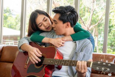 Genç Asyalı çift, Evdeki Oturma Odasında Birlikte Gitar Çalıyor ve Şarkı Söylüyor. Müzik ve Yaşam Tarzı kavramı.