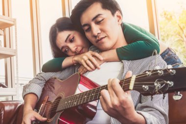 Genç Asyalı çift, Evdeki Oturma Odasında Birlikte Gitar Çalıyor ve Şarkı Söylüyor. Müzik ve Yaşam Tarzı kavramı.