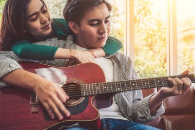 Genç Asyalı çift, Evdeki Oturma Odasında Birlikte Gitar Çalıyor ve Şarkı Söylüyor. Müzik ve Yaşam Tarzı kavramı.