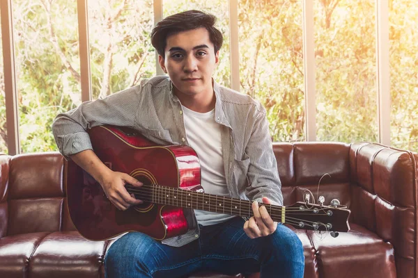 Young guitar player holding his guitar at home. Music and song concept.