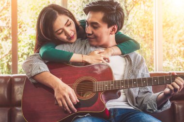 Genç Asyalı çift, Evdeki Oturma Odasında Birlikte Gitar Çalıyor ve Şarkı Söylüyor. Müzik ve Yaşam Tarzı kavramı.