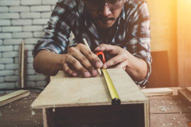 Marangoz atölyede ahşap işçiliği yapıyor. İnşaat malzemesi ya da ahşap mobilya üretiyor. Genç Asyalı marangoz zanaat için profesyonel araçlar kullanır. DIY üreticisi ve marangozluk konsepti.