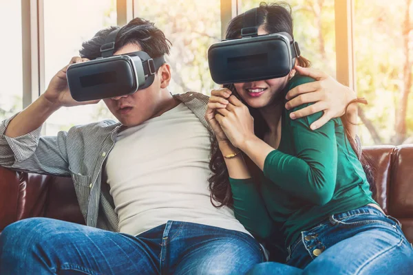 Happy couple watching video in virtual reality VR headset in living room at home. Multimedia movie and entertainment concept.