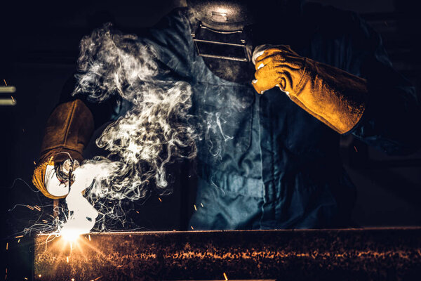 Metal welder working with arc welding machine to weld steel at factory while wearing safety equipment. Metalwork manufacturing and construction maintenance service by manual skill labor concept.