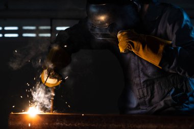 Fabrikada çelik kaynak makinesiyle çalışan metal kaynakçı güvenlik ekipmanı takıyor. El becerisi iş gücü kavramına göre metal imalatı ve inşaat bakım hizmeti.