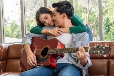 Genç Asyalı çift, Evdeki Oturma Odasında Birlikte Gitar Çalıyor ve Şarkı Söylüyor. Müzik ve Yaşam Tarzı kavramı.