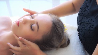 Lüks bir spa merkezinde masaj terapisti tarafından yüz masajı ve spa tedavisi için kaplıcaya uzanmış rahat bir kadın. Sağlık, stres atma ve gençleştirme kavramı.