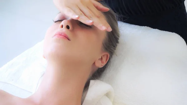 Relaxed woman lying on spa bed for facial and head massage spa treatment by massage therapist in a luxury spa resort. Wellness, stress relief and rejuvenation concept.