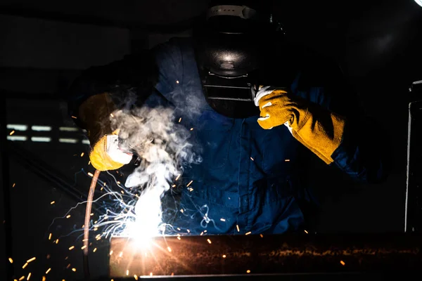 Metal welder working with arc welding machine to weld steel at factory while wearing safety equipment. Metalwork manufacturing and construction maintenance service by manual skill labor concept.