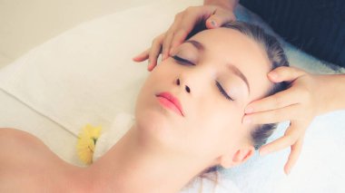Lüks bir spa merkezinde masaj terapisti tarafından yüz masajı ve spa tedavisi için kaplıcaya uzanmış rahat bir kadın. Sağlık, stres atma ve gençleştirme kavramı.