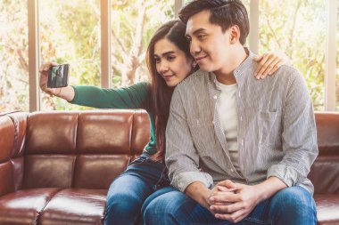 Mutlu Asyalı çift evdeki oturma odasında cep telefonuyla selfie çekmeyi sever..