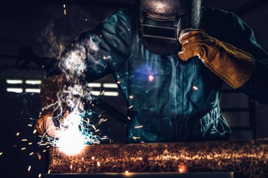 Fabrikada çelik kaynak makinesiyle çalışan metal kaynakçı güvenlik ekipmanı takıyor. El becerisi iş gücü kavramına göre metal imalatı ve inşaat bakım hizmeti.