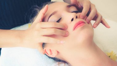 Lüks bir spa merkezinde masaj terapisti tarafından yüz masajı ve spa tedavisi için kaplıcaya uzanmış rahat bir kadın. Sağlık, stres atma ve gençleştirme kavramı.
