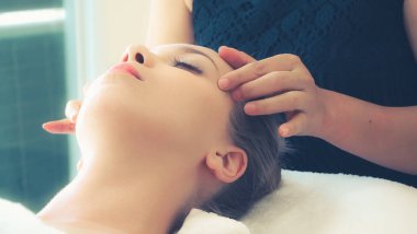 Lüks bir spa merkezinde masaj terapisti tarafından yüz masajı ve spa tedavisi için kaplıcaya uzanmış rahat bir kadın. Sağlık, stres atma ve gençleştirme kavramı.