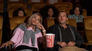 Seyirciler sinema salonundaki koltuklara yürüyor, film izliyor ve patlamış mısır yiyor..