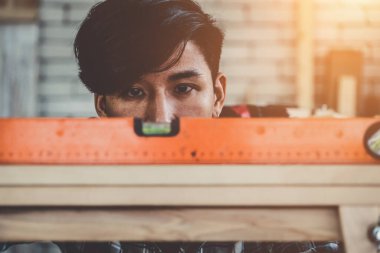 Marangoz atölyede ahşap işçiliği yapıyor. İnşaat malzemesi ya da ahşap mobilya üretiyor. Genç Asyalı marangoz zanaat için profesyonel araçlar kullanır. DIY üreticisi ve marangozluk konsepti.