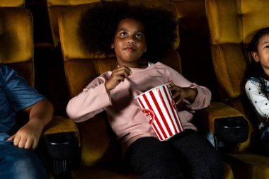 Üç çocuk eğleniyor ve sinemada film izlemekten zevk alıyor.