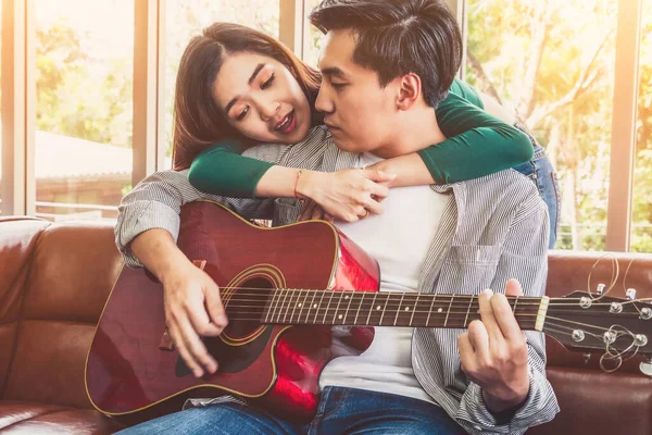 Young Asian Couple Plays Guitar and Sing Song in Living Room at Home Together. Music and Lifestyle concept.