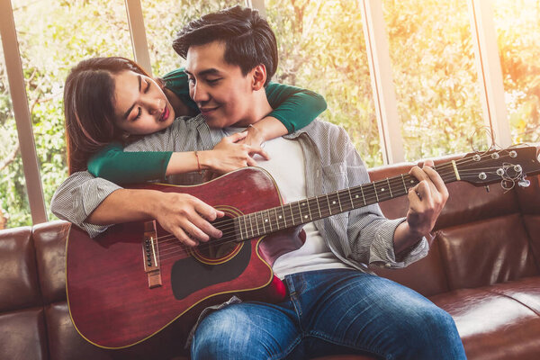 Young Asian Couple Plays Guitar and Sing Song in Living Room at Home Together. Music and Lifestyle concept.