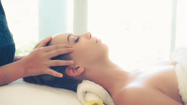 Relaxed woman lying on spa bed for facial and head massage spa treatment by massage therapist in a luxury spa resort. Wellness, stress relief and rejuvenation concept.