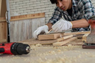 Marangoz atölyede ahşap işçiliği yapıyor. İnşaat malzemesi ya da ahşap mobilya üretiyor. Genç Asyalı marangoz zanaat için profesyonel araçlar kullanır. DIY üreticisi ve marangozluk konsepti.