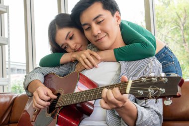 Genç Asyalı çift, Evdeki Oturma Odasında Birlikte Gitar Çalıyor ve Şarkı Söylüyor. Müzik ve Yaşam Tarzı kavramı.