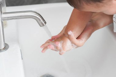 Anne, Coronavirus Hastalığı 2019 ya da COVID-19 'u önlemek için bebek elini yıkıyor. İnsanlar virüs enfeksiyonunu temizlemek için lavaboda ellerini yıkıyor..