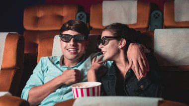 Sinemada üç boyutlu gözlüklü bir kadın ve erkek film izliyor. Ekrana bakar, heyecan verici ve patlamış mısır yer.