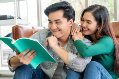 Genç Asyalı çift oturma odasında kitap okuyor. Aşk ilişkisi ve yaşam tarzı kavramı.