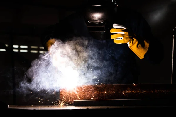 Metal welder working with arc welding machine to weld steel at factory while wearing safety equipment. Metalwork manufacturing and construction maintenance service by manual skill labor concept.