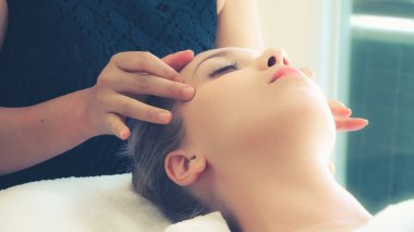 Lüks bir spa merkezinde masaj terapisti tarafından yüz masajı ve spa tedavisi için kaplıcaya uzanmış rahat bir kadın. Sağlık, stres atma ve gençleştirme kavramı.