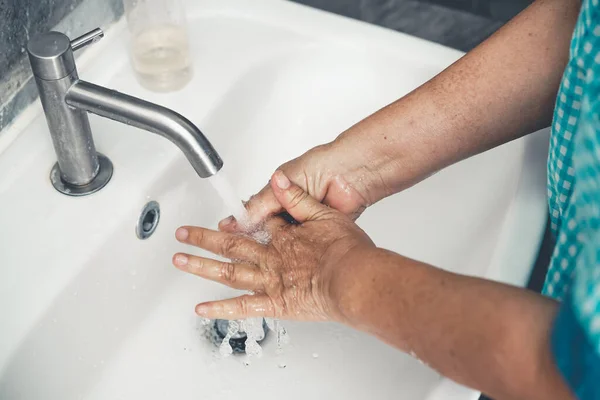 Senior woman wash hand for prevention of novel Coronavirus Disease 2019 or COVID-19 . People wash hands at bathroom sink to clean the virus infection.