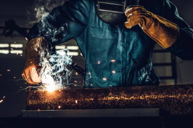 Fabrikada çelik kaynak makinesiyle çalışan metal kaynakçı güvenlik ekipmanı takıyor. El becerisi iş gücü kavramına göre metal imalatı ve inşaat bakım hizmeti.