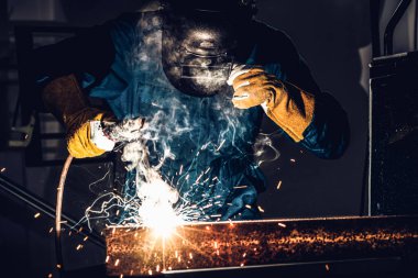Fabrikada çelik kaynak makinesiyle çalışan metal kaynakçı güvenlik ekipmanı takıyor. El becerisi iş gücü kavramına göre metal imalatı ve inşaat bakım hizmeti.