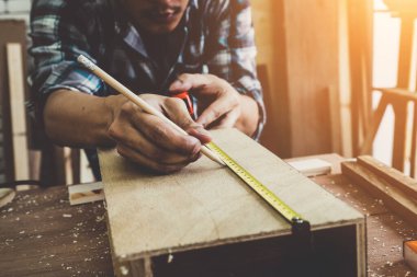 Marangoz atölyede ahşap işçiliği yapıyor. İnşaat malzemesi ya da ahşap mobilya üretiyor. Genç Asyalı marangoz zanaat için profesyonel araçlar kullanır. DIY üreticisi ve marangozluk konsepti.