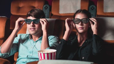Sinemada üç boyutlu gözlüklü bir kadın ve erkek film izliyor. Ekrana bakar, heyecan verici ve patlamış mısır yer.