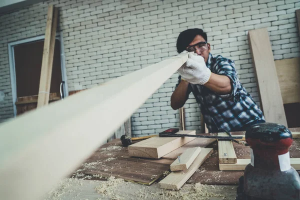 Carpenter working on wood craft at workshop to produce construction material or wooden furniture. The young Asian carpenter use professional tools for crafting. DIY maker and carpentry work concept.